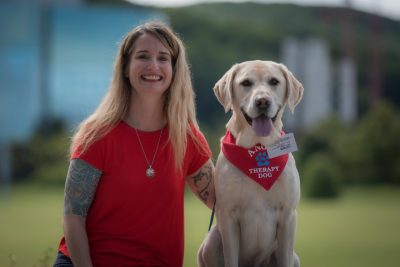 Woman sitting with dog wearing a scarf that says "Therapy Dog."